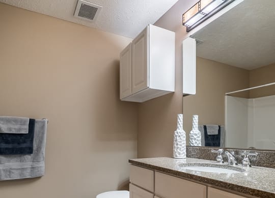 a bathroom with white cabinets, granite countertop, and a large mirror with overhead lighting