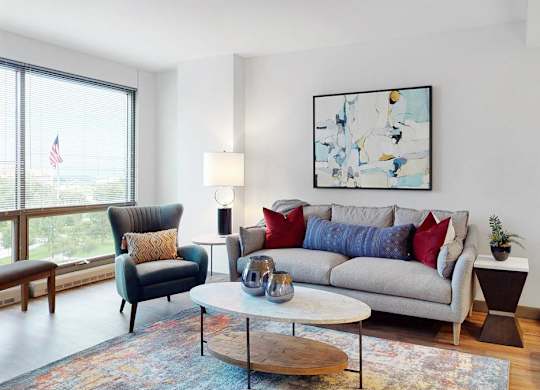A living room with a grey couch, a black chair, a wooden coffee table, and large windows