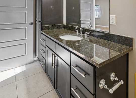 A bathroom with linen cabinets,  under sink storage, light tile floors, and dark brown cabinets