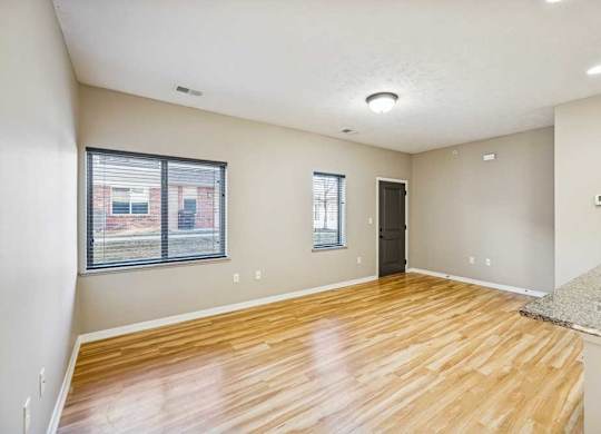 A large living room with wooden floors and large windows. The front door is dark and on the right.