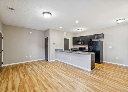 An apartment kitchen with wooden floors, black appliances, and granite countertops..