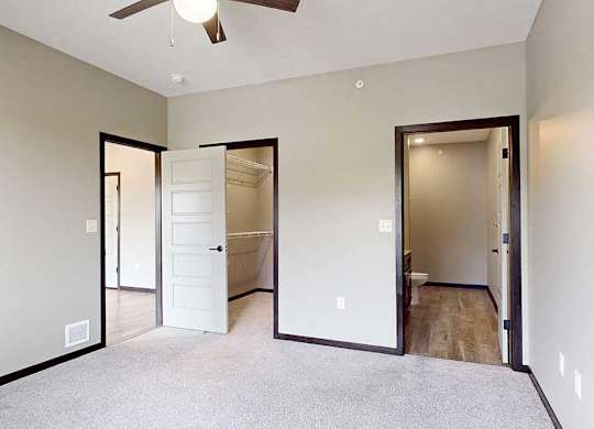 A carpeted bedroom with a ceiling fan, a walk-in closet, and an attached bathroom.