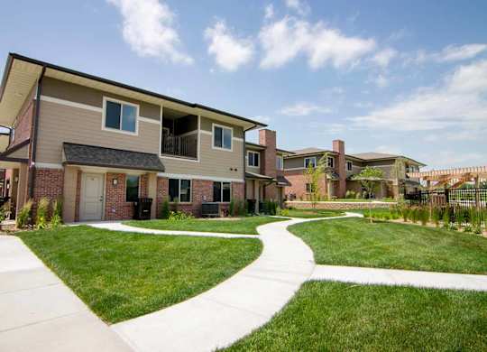 A villa-style apartment building with a green lawn in front of it, and a fenced in pool nearby.
