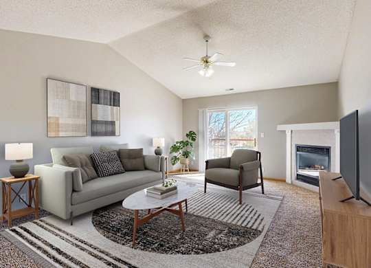 A virtually staged living room with a grey couch, a coffee table, a fireplace, and a television.