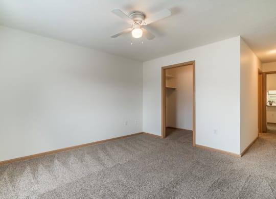 an empty living room with a ceiling fan and a closet