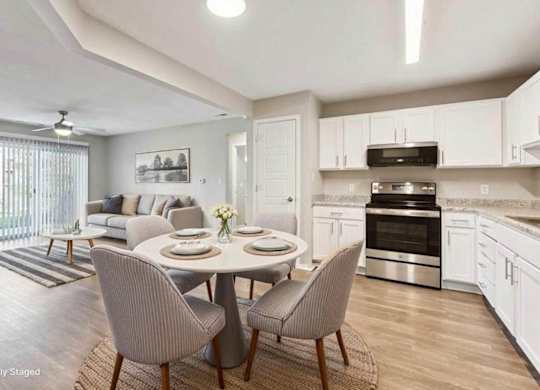 Virtually staged open-concept apartment kitchen and living area with white cabinetry, stainless steel oven, wood-style flooring, and sliding glass doors.