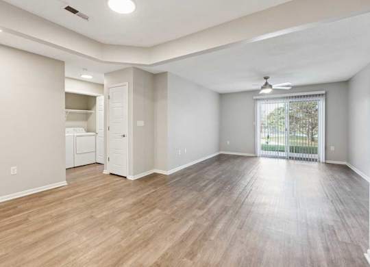 Spacious open living area with wood-style flooring, ceiling fan, sliding glass door to patio, and adjacent laundry closet and storage space.