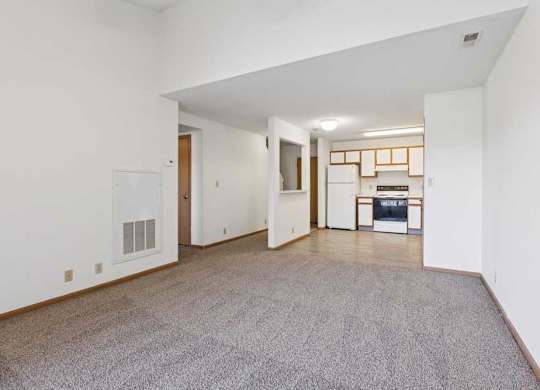 A spacious living room with a grey carpet and white walls.