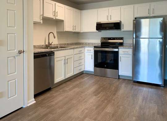 an updated L-shape kitchen with white cabinets, stainless steel appliances, granite countertops, and hardwood flooring