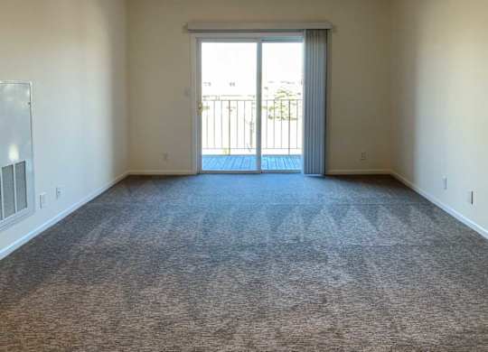 a living room with carpeted flooring and a sliding glass door to a balcony
