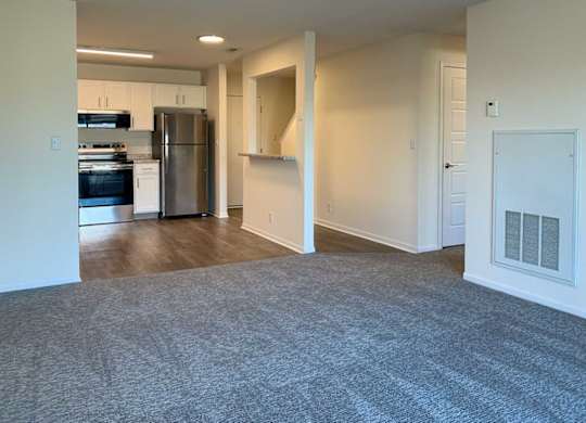 a living room the runs into a kitchen with hardwood floors, stainless steel appliances and white cabients