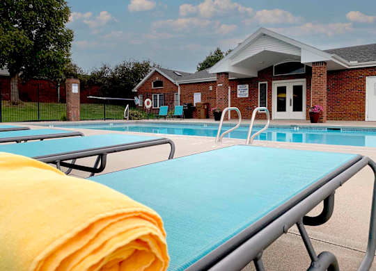 apartment swimming pool with two light blue lounge chairs a clubhouse in the background