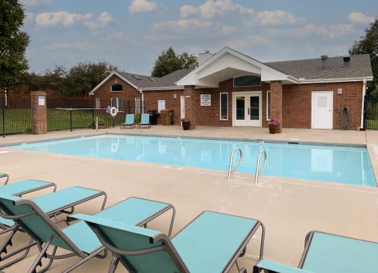a swimming pool with blue chaise lounge chairs and the clubhouse in the background