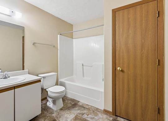 Apartment bathroom with a single-sink vanity, large mirror, toilet, tub/shower combination, and durable flooring with neutral finishes throughout.