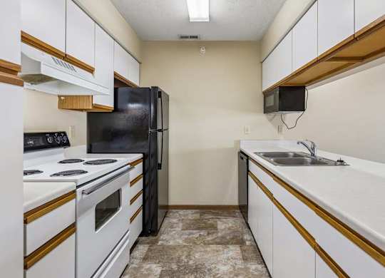 Galley-style apartment kitchen with white cabinets, white oven, black refrigerator, laminate countertops, a double-basin sink, and durable flooring in a functional layout.