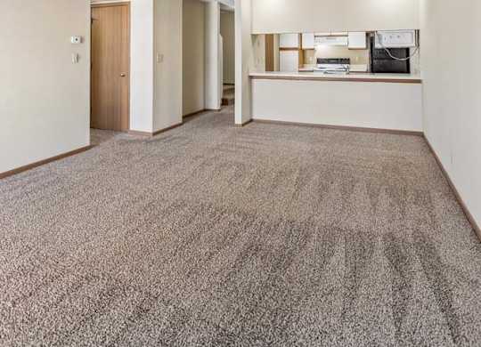 Spacious apartment living room with vaulted ceilings, neutral carpet, and an open-concept layout featuring a breakfast bar overlooking the kitchen.
