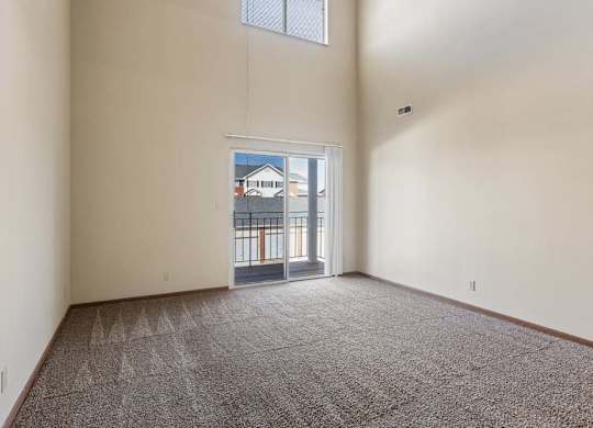 Spacious apartment living room with vaulted ceilings, neutral carpet, and a large sliding glass door with a transom window that fills the space with natural light.