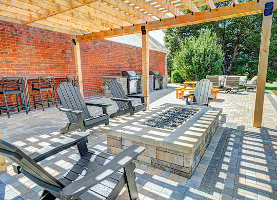 A patio with a pergola covering a fire pit with surrounding chairs.