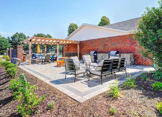 An outdoor patio with social seating areas, a picnic table, grilling stations, a fire pit, and a pergola.