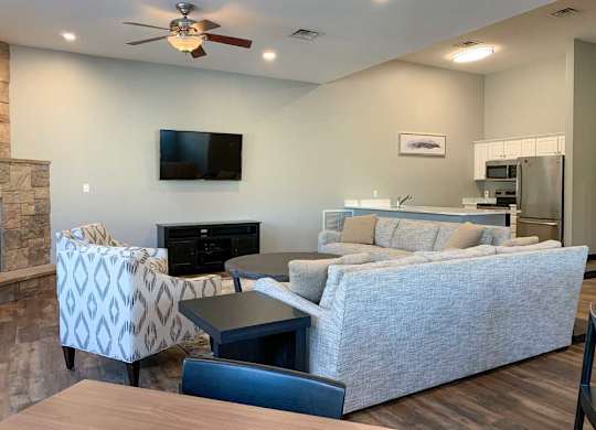 a clubhouse living room with a grey couch, a black television, and a stone fireplace