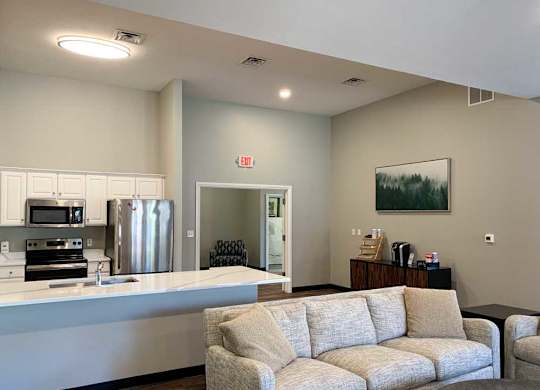a modern kitchen with white cabinets and stainless steel appliances in a clubhosue with a coffee bar and grey couch