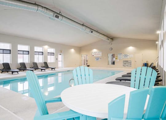 an indoor swimming pool with lounge chairs and a nearby table