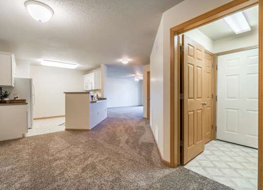 A kitchen with white cabinets and a refrigerator is visible through an open door.