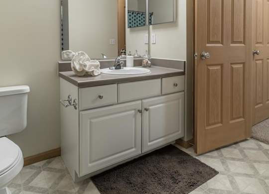 A bathroom with a white toilet, a sink with a mirror above it, and a brown door.