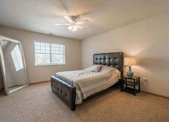 A bedroom with a bed, a nightstand, and a ceiling fan.