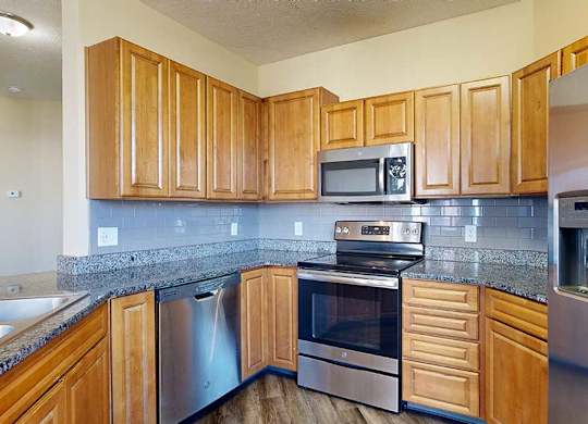 a kitchen with granite countertops, wooden cabinets, a tile backsplash, and stainless steel appliances