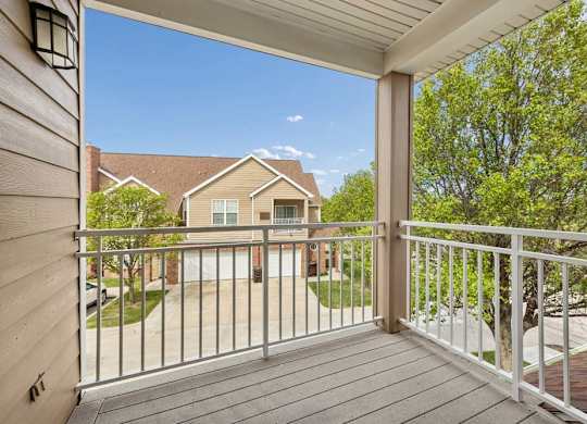 Covered apartment balcony with sliding glass doors, tan siding, white entry door, and outdoor wall light.