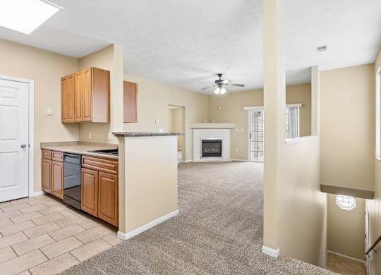 Open apartment interior with kitchen, carpeted living room, fireplace, windows, and stairway landing.