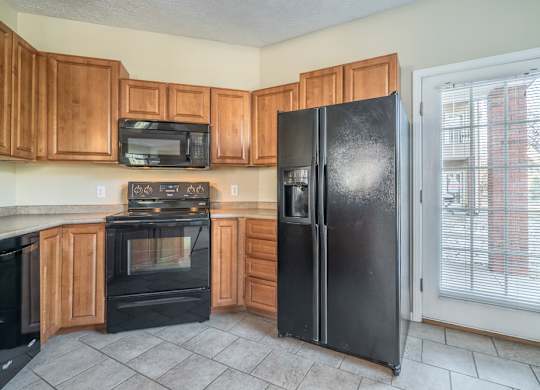 A kitchen with warm cabinetry, black appliances, and a door to a patio space.