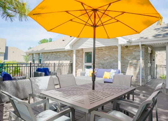 outdoor dining table and chairs shaded with a yellow umbrella on the sun deck of the community clubhouse