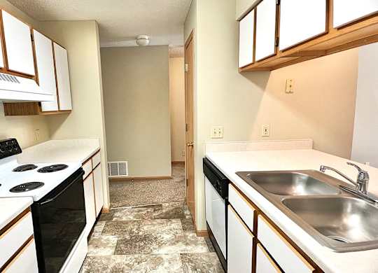 Galley style kitchen with white cabinets and oak trim, white appliances, and tan vinyl flooring