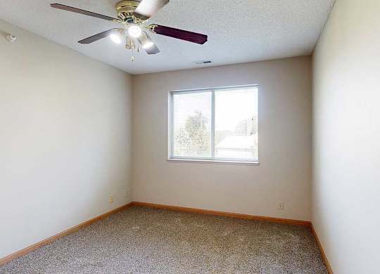 Bright bedroom with neutral walls, plush carpet, ceiling fan with light, and window for natural light.