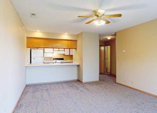 Open-concept living and dining area with plush carpet, ceiling fan, and breakfast bar to the kitchen.