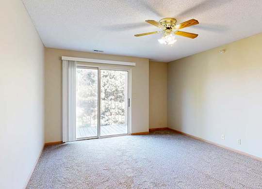 Spacious living room with sliding glass door to balcony, neutral walls, and ceiling fan with light.