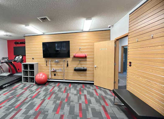 a 24-hour fitness center with treadmills, TVs, yoga equipment, and wooden paneling on the walls