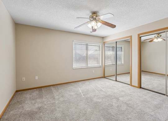 Spacious bedroom with mirrored closet doors, carpet flooring, and ceiling fan.