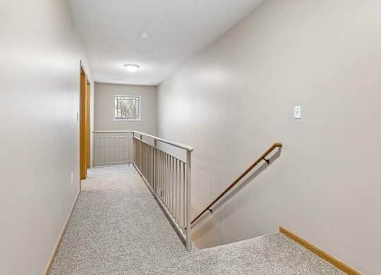 Upstairs hallway with carpeted flooring, railing overlook, and staircase.
