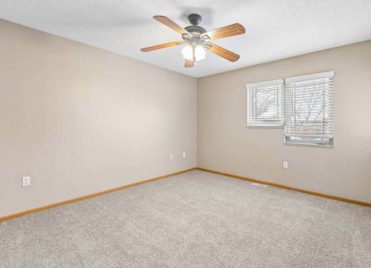 Carpeted bedroom with ceiling fan and window.