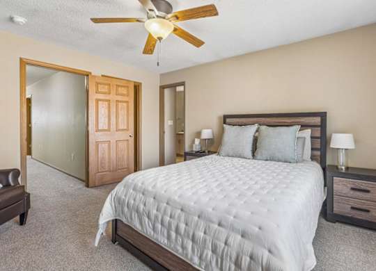 A bedroom with a large bed, a ceiling fan, and a nightstand with a lamp.