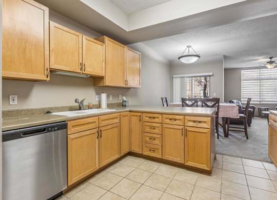 Open apartment kitchen with light wood cabinets, tile flooring, ample counter space, and adjacent dining area.