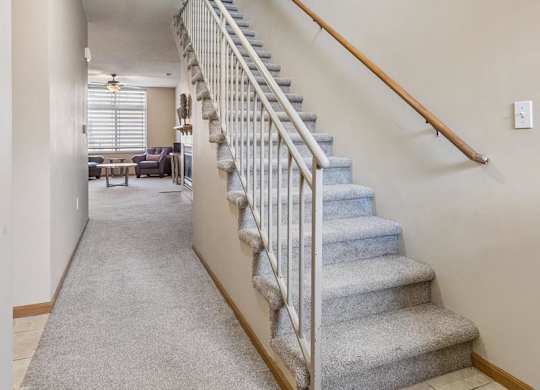 Apartment entry hallway with carpeted staircase, neutral finishes, and open layout leading to the main living area.