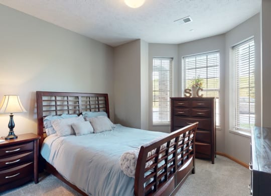 a bedroom with a bed and a dresser brightened with natural light from windows