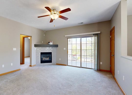 a living room with a fireplace, sliding glass doors to a balcony, and a ceiling fan