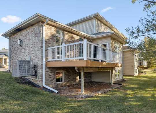 Rear duplex exterior with elevated deck, white railing, brick and siding facade, and backyard lawn.