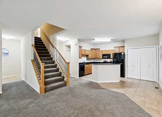 Open-concept living space with staircase, carpet and tile flooring, and kitchen with peninsula seating.