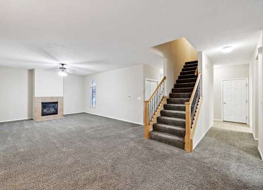 Open living space featuring staircase, fireplace, and wide carpeted area for flexible furniture layout.